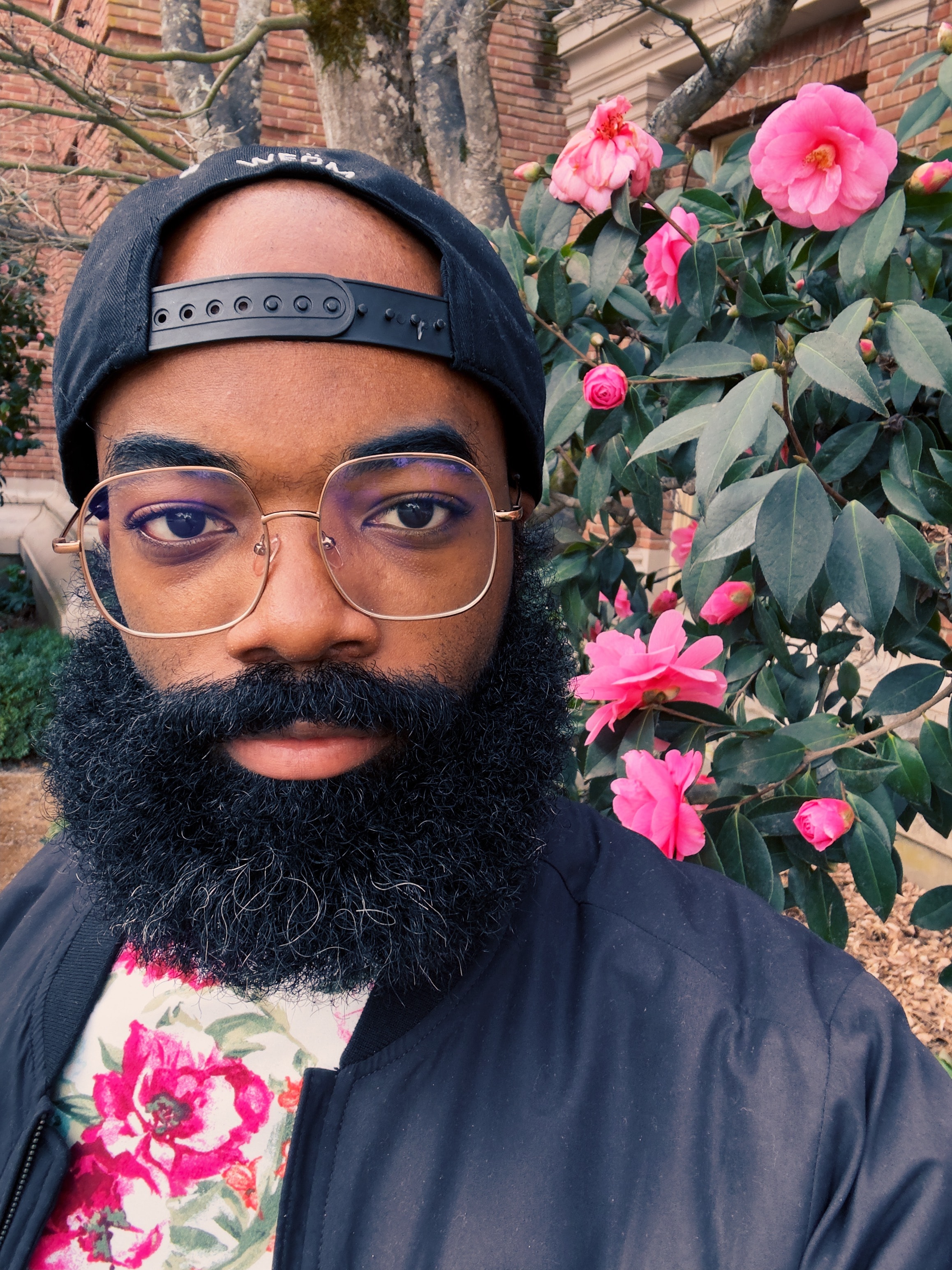 Paul Anthony Webb in front of a flower bush whilst wearing a floral shirt in similar rich pink color